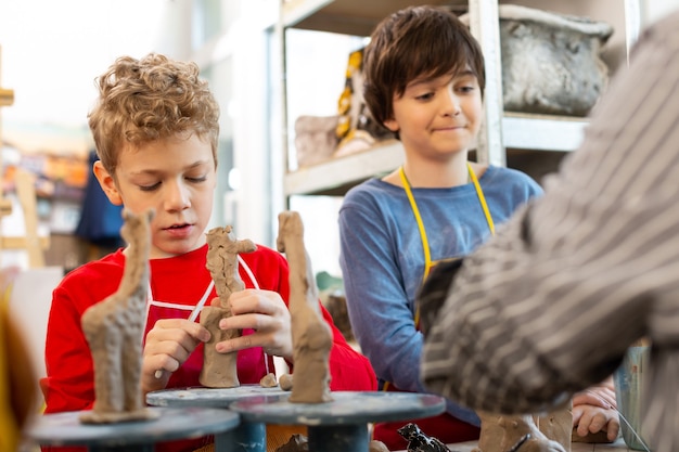 Foto due ragazzi di talento che modellano animali di argilla alla lezione di arte