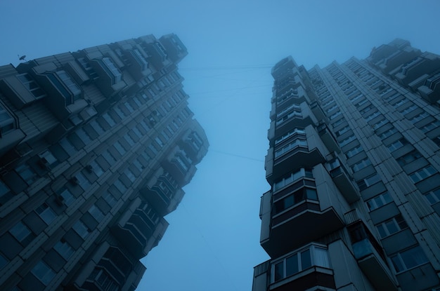 Two tall residential buildings immersed in misty sky Cyberpunk stylistics