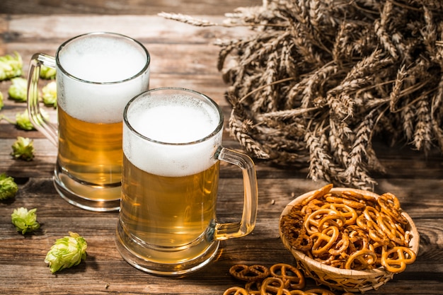 Due boccali di birra, spighe, hop sul tavolo di legno