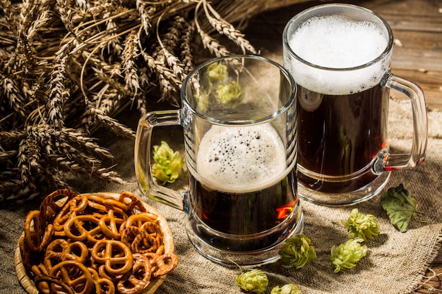 Two tankard beer with wheat and hops , basket of pretzels