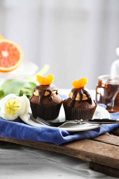Photo two tasty cupcakes with slice of mandarin and chocolate on a plate over light wooden background