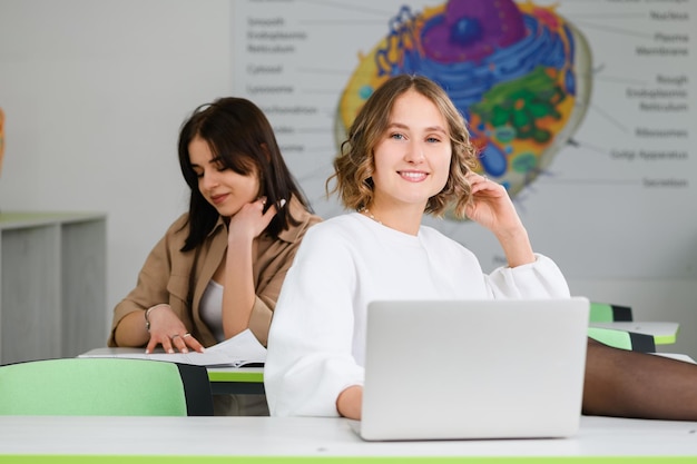 Two teenage female friends study at high school with paper notebook and laptop at lecture class room