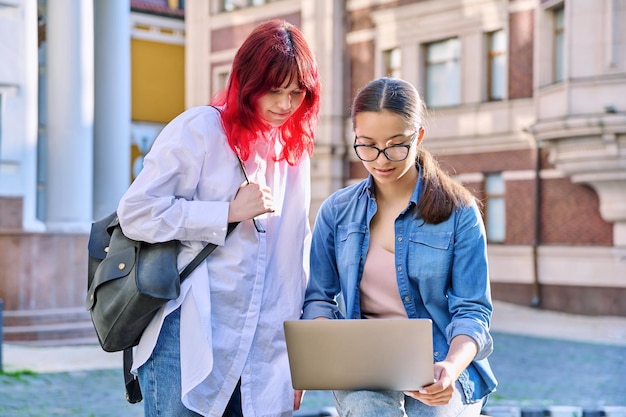 Two teenage female students using outdoor laptop city street background