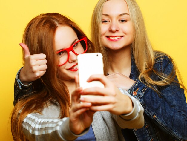 Due amici di ragazze adolescenti in attrezzatura hipster fanno selfie su un telefono