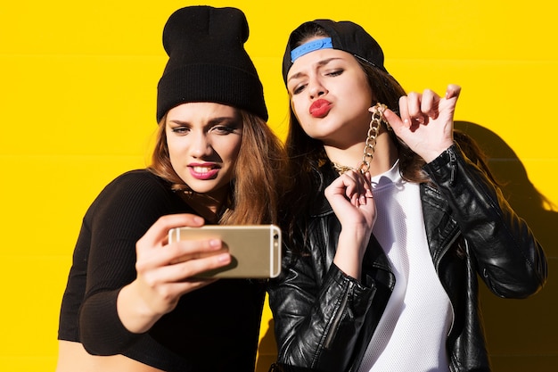 Due amiche adolescenti in abito hipster all'aperto fanno selfie su un telefono.