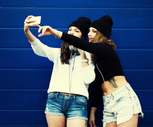 Two teenage girls friends in hipster outfit outdoors make selfie on a phone.