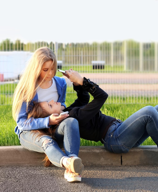 Two teenage girls using smartphone taking a selfie sitting together Two girls laughing and grimacing