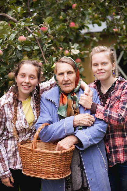 Two teenage girls with grandmother in apple orchard with basketxDxA