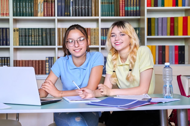 Two teenage schoolgirls students sitting with a laptop in the library