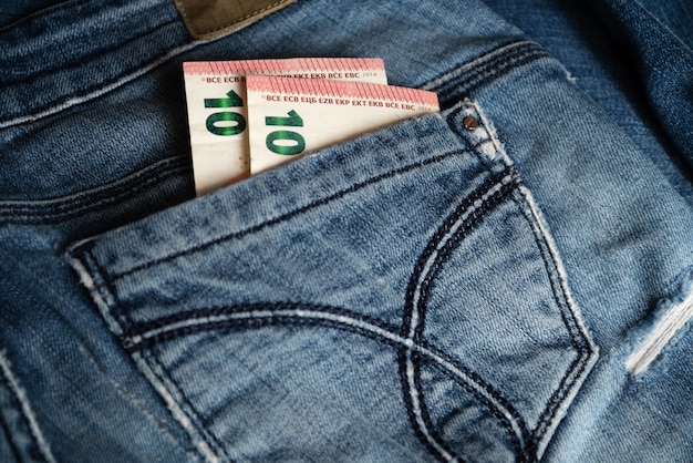 Two of ten euro banknotes peek out from back pocket of old blue jeans