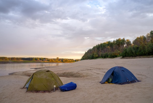 Two tents on the sand near the river at sunrise rest after fishing Fisherman's camp on the river
