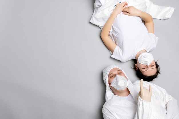 Two tired doctor male and female in a protective suit on the floor exhausted in the fight against a ...