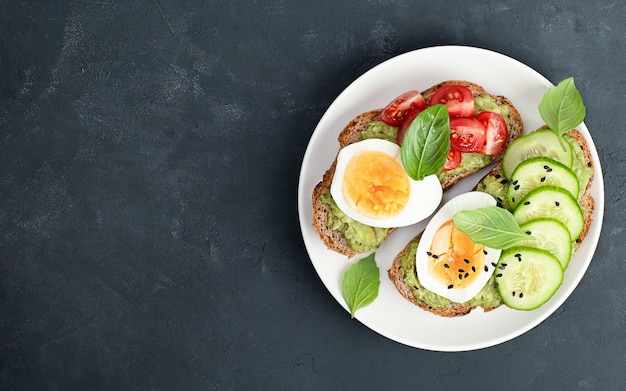 Two toast breads with vegetables, egg and basil on a plate on a black concrete table