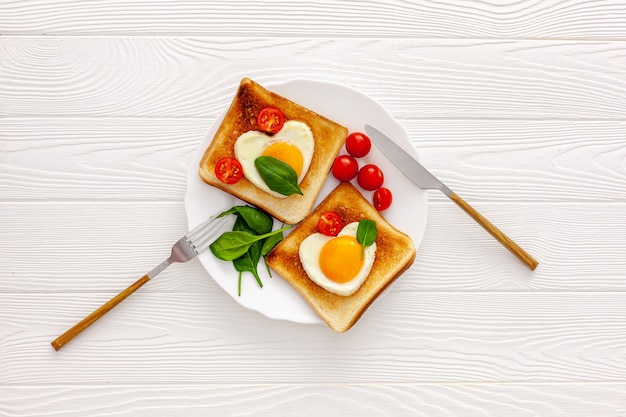 Two toast with scrambled eggs in the shape of a heart on a plate