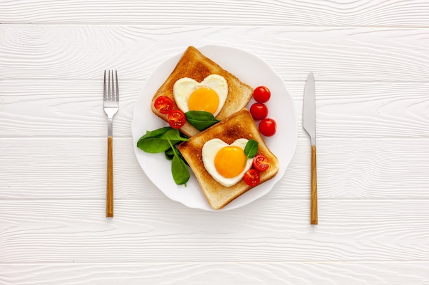 Two toast with scrambled eggs in the shape of a heart on a plate