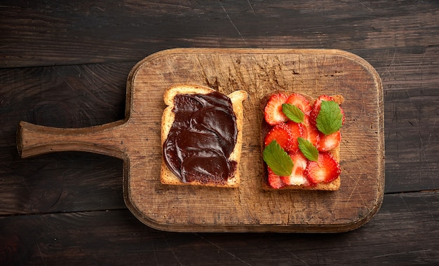 Due toast con pasta di cioccolato e fragole rosse mature fresche su una tavola di legno marrone