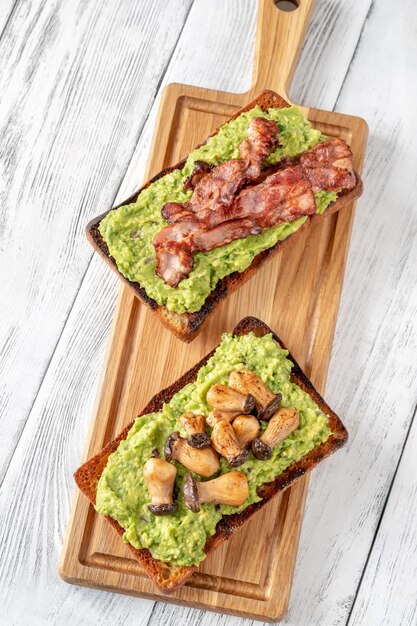 Two toasts with guacamole mushrooms and bacon on cutting board