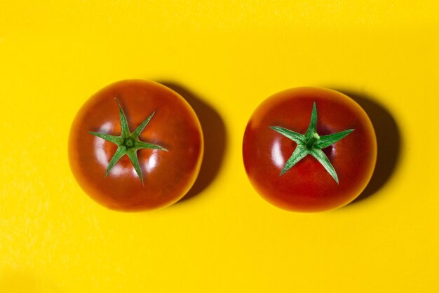 Photo two tomatoes with green tails isolated on yellow background