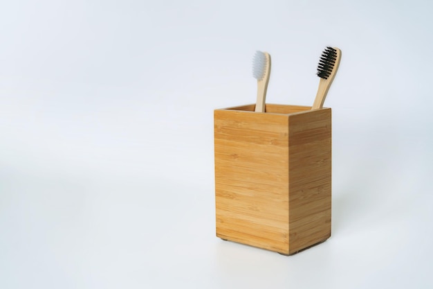 Two toothbrushes in bamboo holder on white background