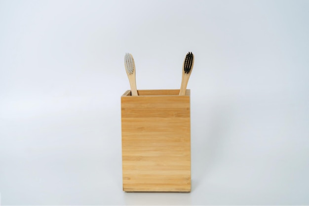 Two toothbrushes in bamboo holder on white background