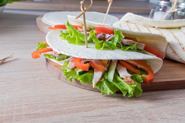 Two tortillas of stuffed with fresh vegetables and chicken fillets on a cutting board and a wooden table food trend Fashionable way of wrapping