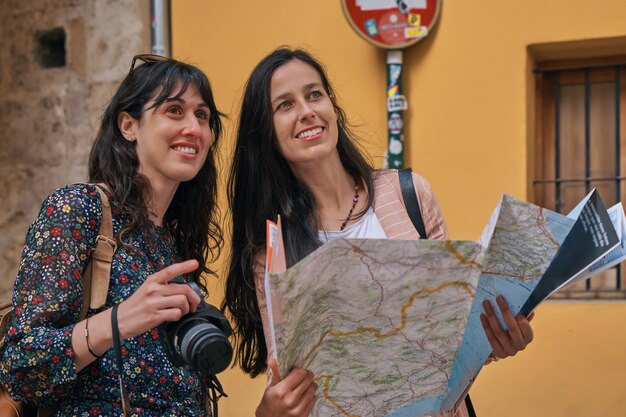 Two tourist girls walking through the city streets on vacation holding a map