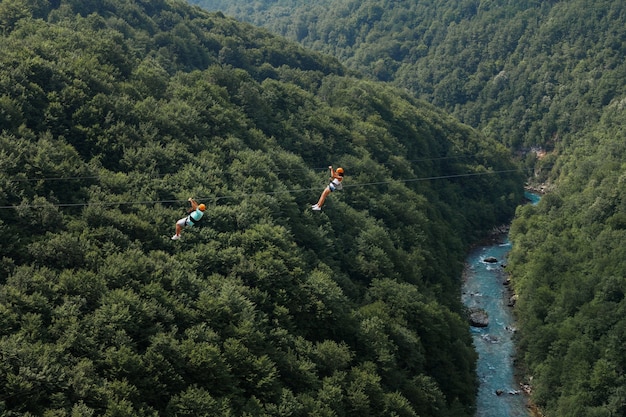 緑の山々と川を背景にジップラインで2人の観光客