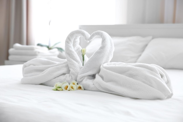 Два лебедя из полотенец и цветы на белом постельном белье