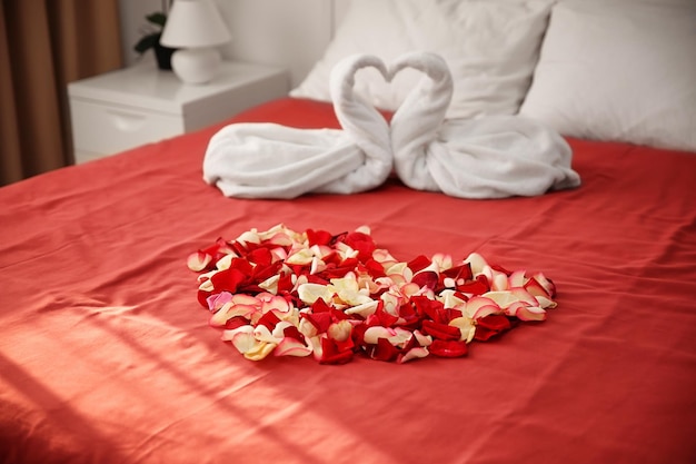 Two towel swans and rose petals on bed in hotel room