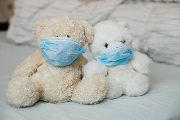 Two toy bears with medical masks on bed. Sicker disease in children. Coronovirus, quarantine, epidemic, pandemic, cold,illness. Medicine concept and health.