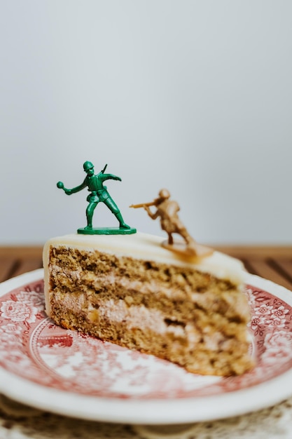 Photo two toy soldiers fighting on the top of a piece of cake on a plate - white background - close up