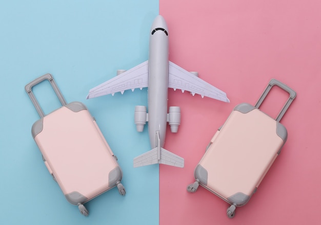 Two toy travel luggage and air plane on pink blue pastel. Travel planning