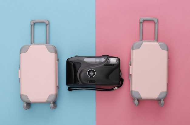 Two toy travel luggage and camera on pink blue pastel. Travel planning