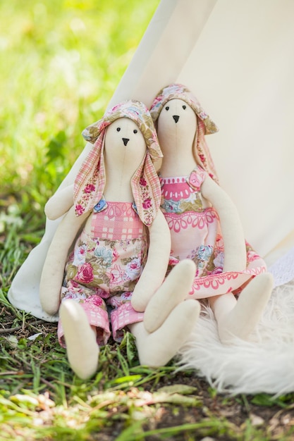 Two toys rabbits a boy and a girl hand made in the style of Tilda are sitting in nature at the base of the tent