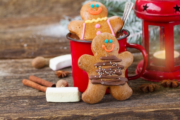 Two traditional homemade gingerbread men on wooden table with chocolate in red mug