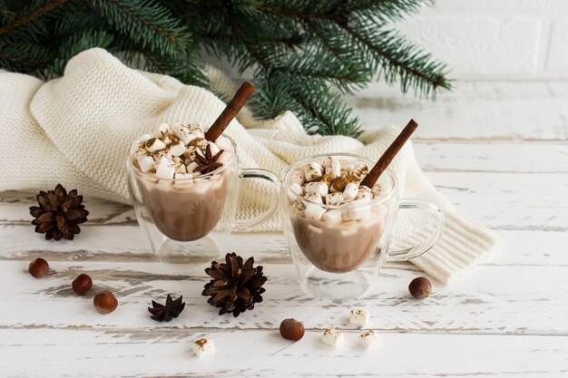 Due tazze trasparenti con doppio fondo con cioccolata calda e marshmallow su fondo di legno bianco. il concetto vacanze di capodanno.