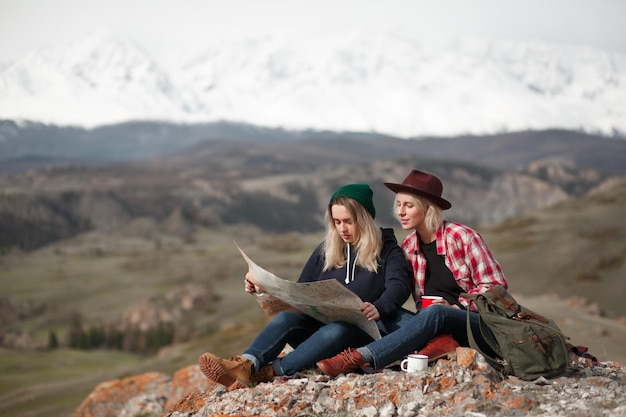 사진 산의 바위 위에 앉아 있는 지도를 가진 두 명의 여행자 소녀