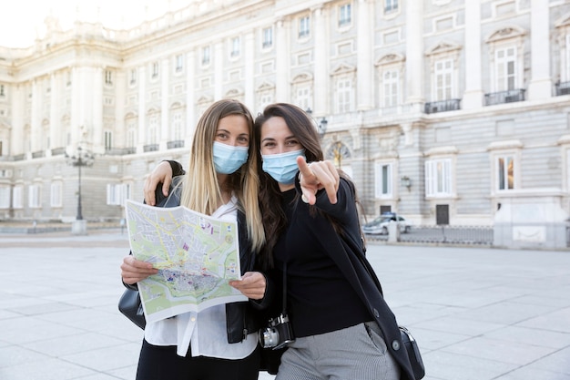 Two traveling friends pointing in the direction they are looking. They are wearing medical masks. Concept of travel and new normal.