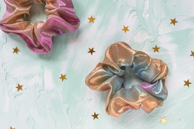 Two trendy holographic scrunchies and golden stars confetti on green table