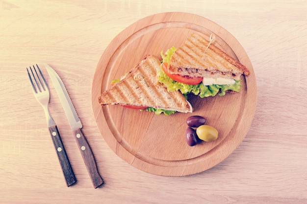 Two triangular sandwiches and olives on a wooden round Board