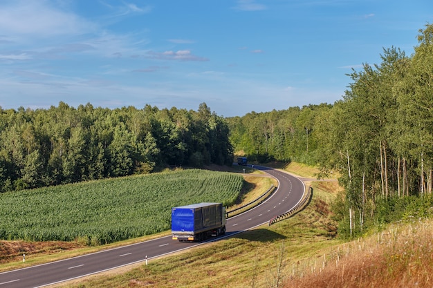 Two trucks are moving towards each other along a bend in the road in a rural area