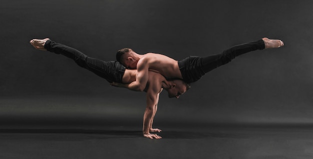 Two twin brothers in black jeans with a naked torso perform acrobatic elements black background