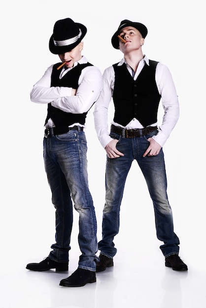 Два брата-близнеца в гангстерском стиле позирует. шапки, жилеты, белые рубашки. белый фон.