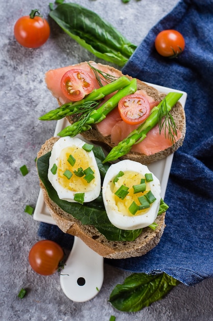 Due tipi di sandwich con spinaci, uova sode e salmone salato, pomodorini, asparagi verdi