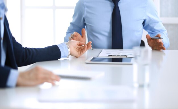 Two unknown businessmen or partners using tablet pc and discussing questions at meeting in modern office, close-up of hands. Group of managers at negotiation or brainstorm. Teamwork, partnership and b