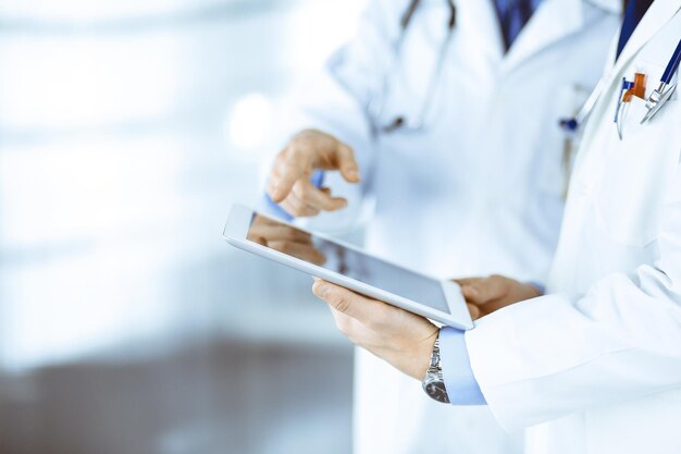 病院のオフィスに立って、聴診器を持った2人の未知の医師が健康診断の結果について話し合っています。医師は、コンピューターのタブレットを使用して薬の名前の記録を記入します。完璧な医療サービスi