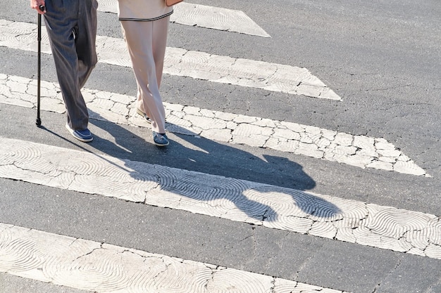 Two unrecognizable elderly people one of them with a cane crossing a pedestrian crossing