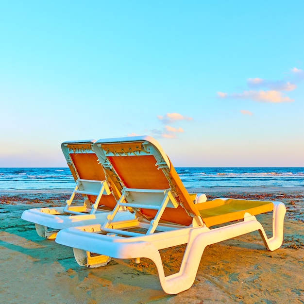 Two vacant deckchairs on a sandy beach