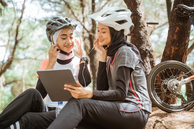 Two veiled girls sitting with earphones on break while cycling