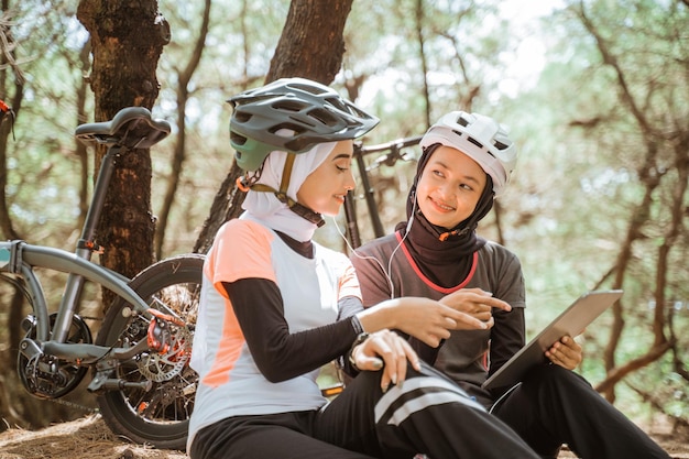 Two veiled girls using tablet and earphones while sitting